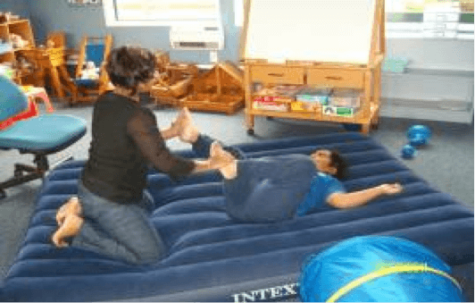 A child and adult pushing on another person rolled in an airbed.