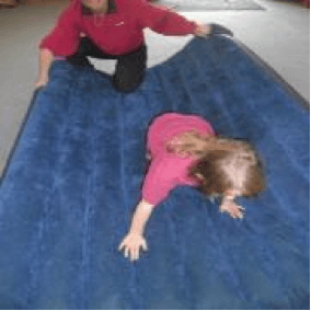 Child crawling on an airbed while the O &amp;amp; M instructor holds and moves the airbed around.