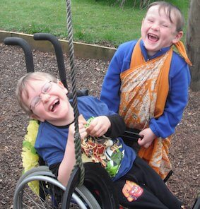 Two young students outside laughing on a swing.
