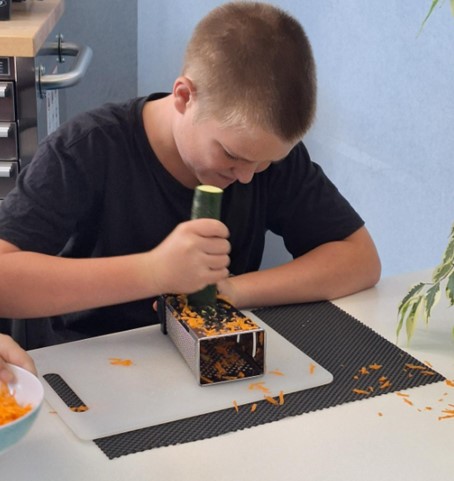 Figure 1 Rico positioning a food grater onto its side and grating the courgette away from his body