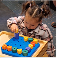 Figure 1 Ripeka is focused on a hands on activity placing colourful geometric shapes onto a blue pegboard as part of her occupation therapy assessment.