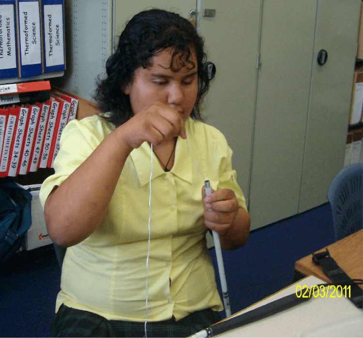 Freedom holding her cane and threading string through with her right hand.