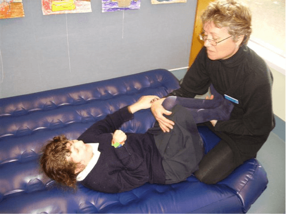 Sam is lying on the airbed with her legs bent up at a 90 degree angle, the O &amp;amp; M Specialist is holding Sam's legs against her stomach.