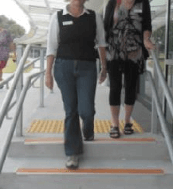 Sighted guide stepping down the first step down and person with vision impairment is standing at the top of the steps.