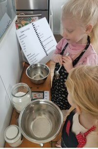 2 girls standing at a bench with their mixing bowls baking.