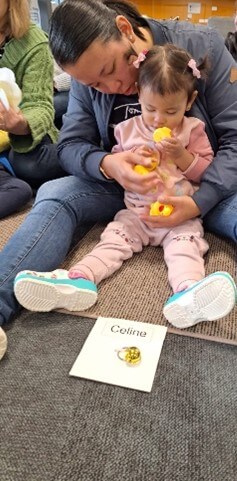 Little girl sitting on mat with mum behind her, feeling plastic yellow ducks.