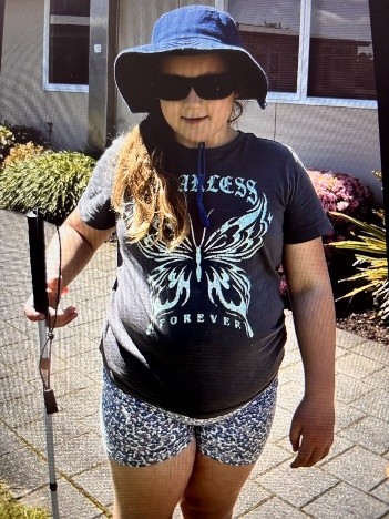 Figure 1 A student standing holding her cane with her hat and NoIR sunglasses on